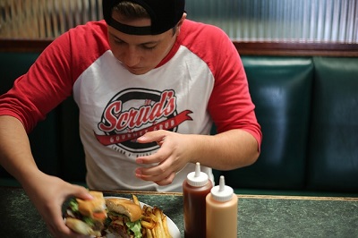 Ob Zoosker das gut finden würden? Hier sehen Sie einen jungen Mann, der einen großen Burger isst.